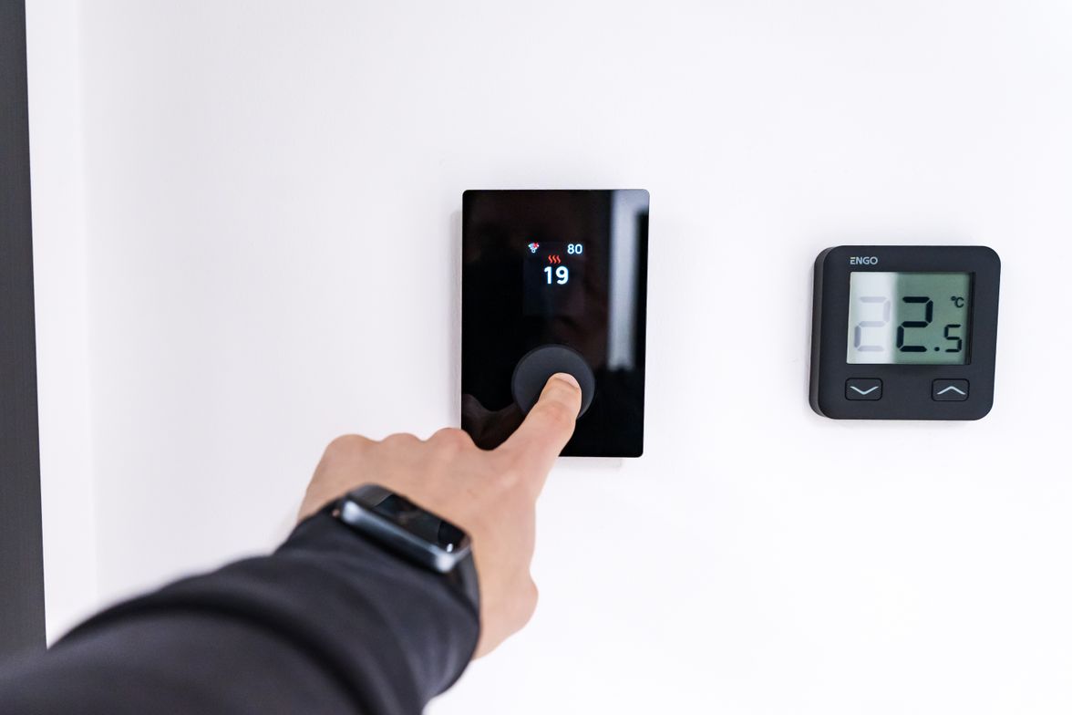 Hand adjusting a digital wall thermostat in a home.