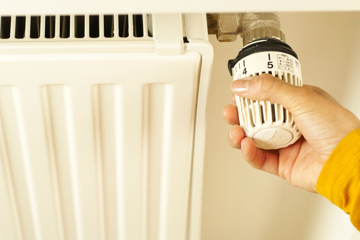 Hand adjusting the thermostatic valve on a home radiator to set the heating temperature.