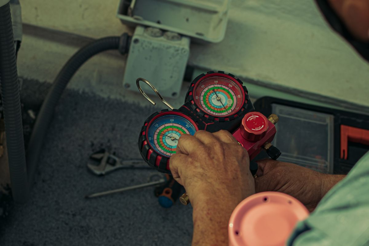 Technician adjusting a refrigerant manifold gauge set during air conditioning service.
